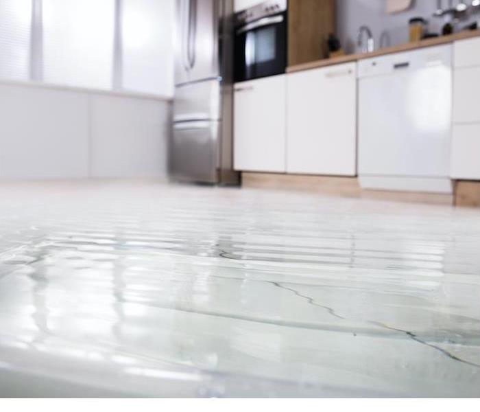 Water pooling on a white tile kitchen floor with white cabinets
