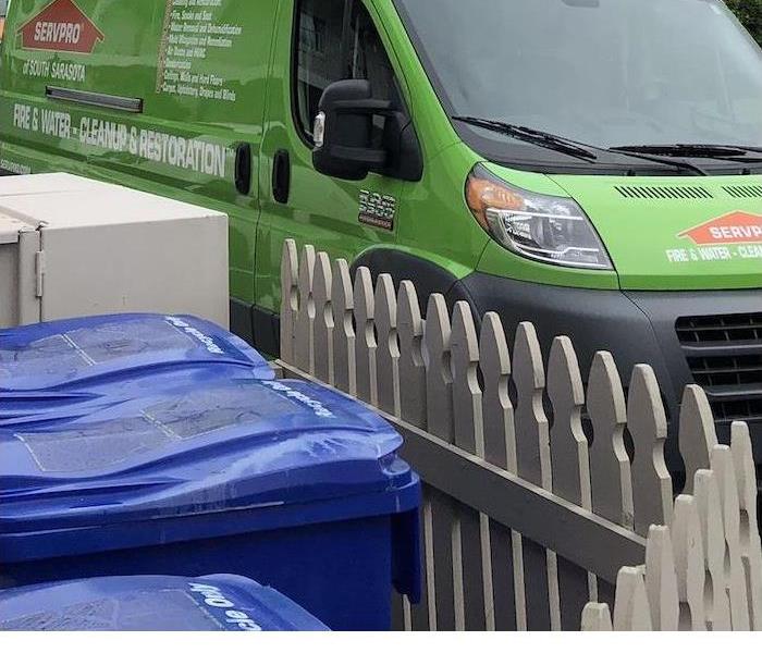 A SERVPRO van parked in front of a tan fence and blue trash cans. 